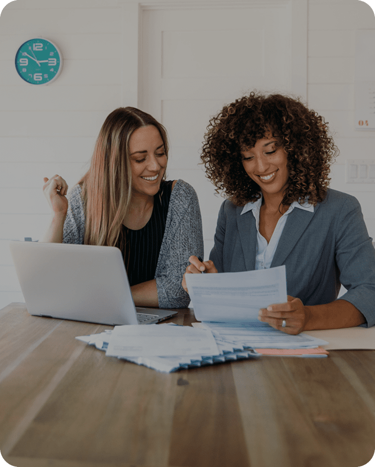 Two women collaborating on work with laptops and documents.